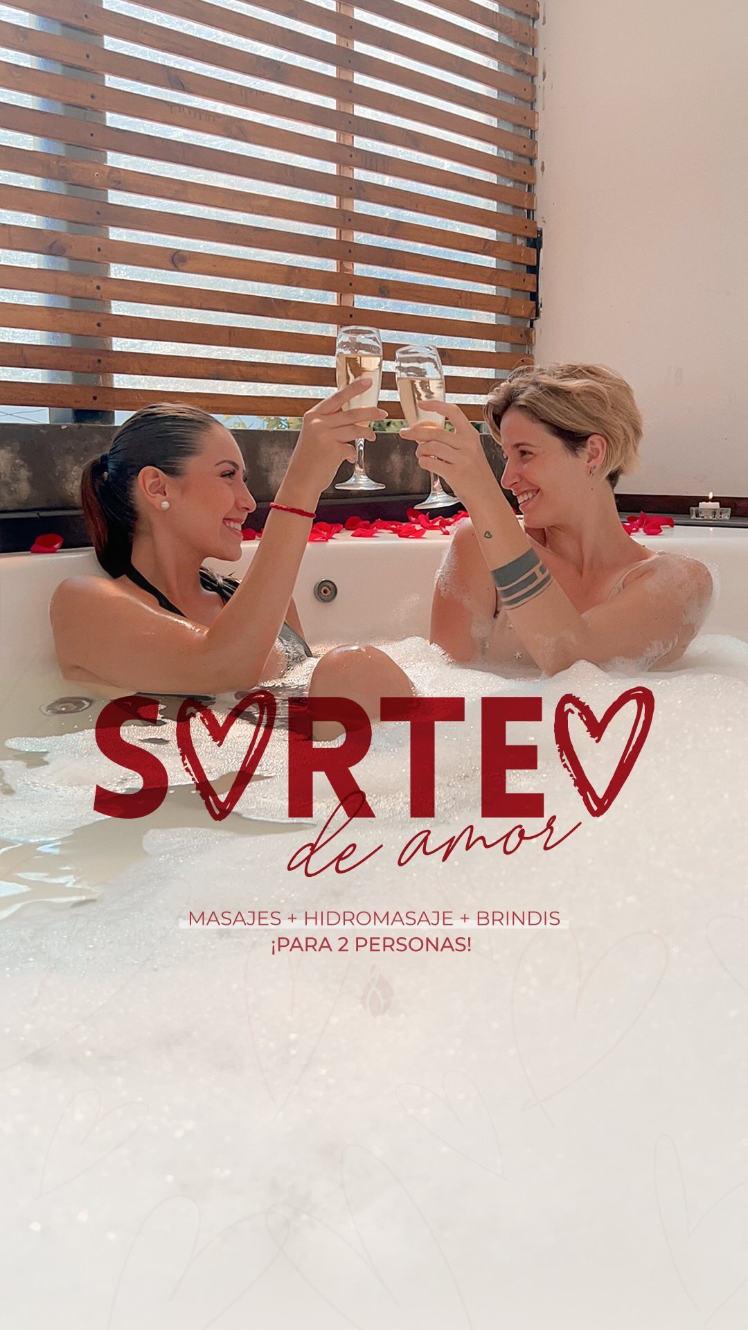 Dos clientas brindando dentro del hidromasaje de Prometeo, con pétalos de rosa sobre el borde y el biombo de listones de madera detrás